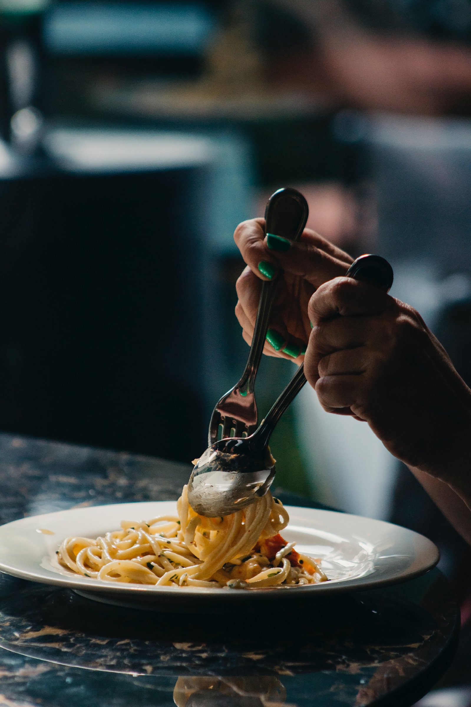 Hands serving pasta on a white plate
