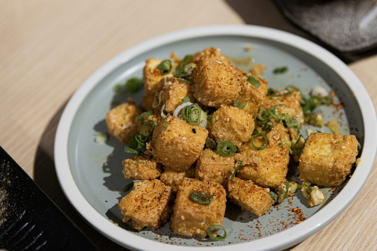 Plate of golden-brown crispy fried tofu cubes garnished with sliced green onions and chili seasoning.