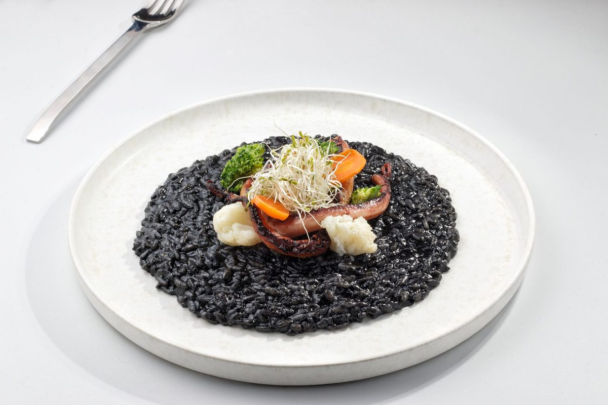 Finished Arroz Negro (Valencian squid rice), a black squid-ink rice dish garnished with vegetables and sprouts
