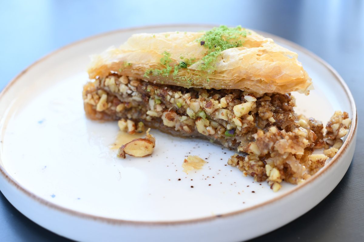 Close-up of a plated slice of baklava with flaky golden pastry layers, chopped nuts, and pistachio topping.