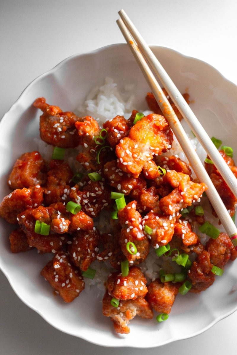 Finished Cantonese crispy fried chicken pieces with sesame and scallions over rice
