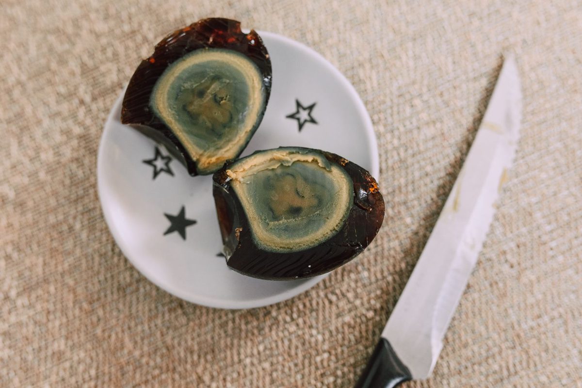 Sliced century eggs arranged on a white plate beside a knife on burlap fabric.