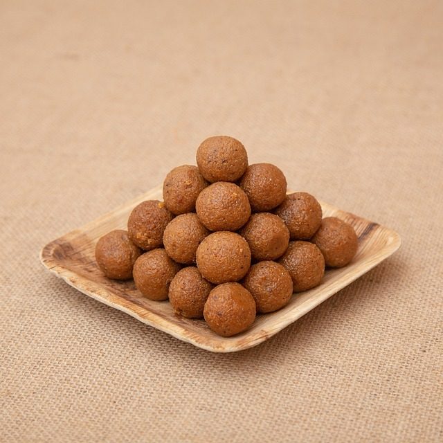 A mound of round golden-brown Indian sweets arranged on a square wooden plate over burlap fabric.