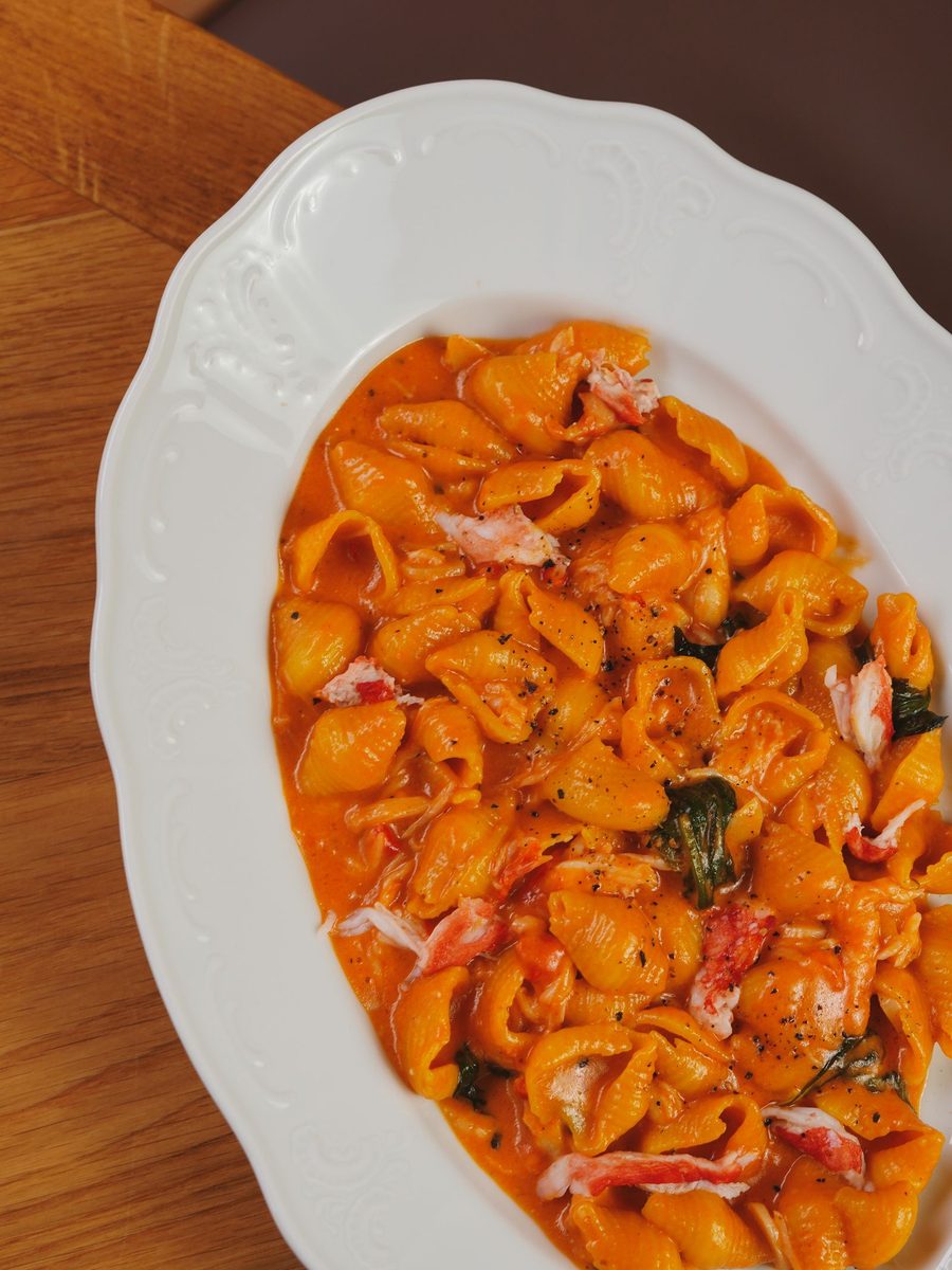 Top-down view of conchiglie pasta in rich tomato sauce, topped with pieces of fresh crab meat, served on a white plate.