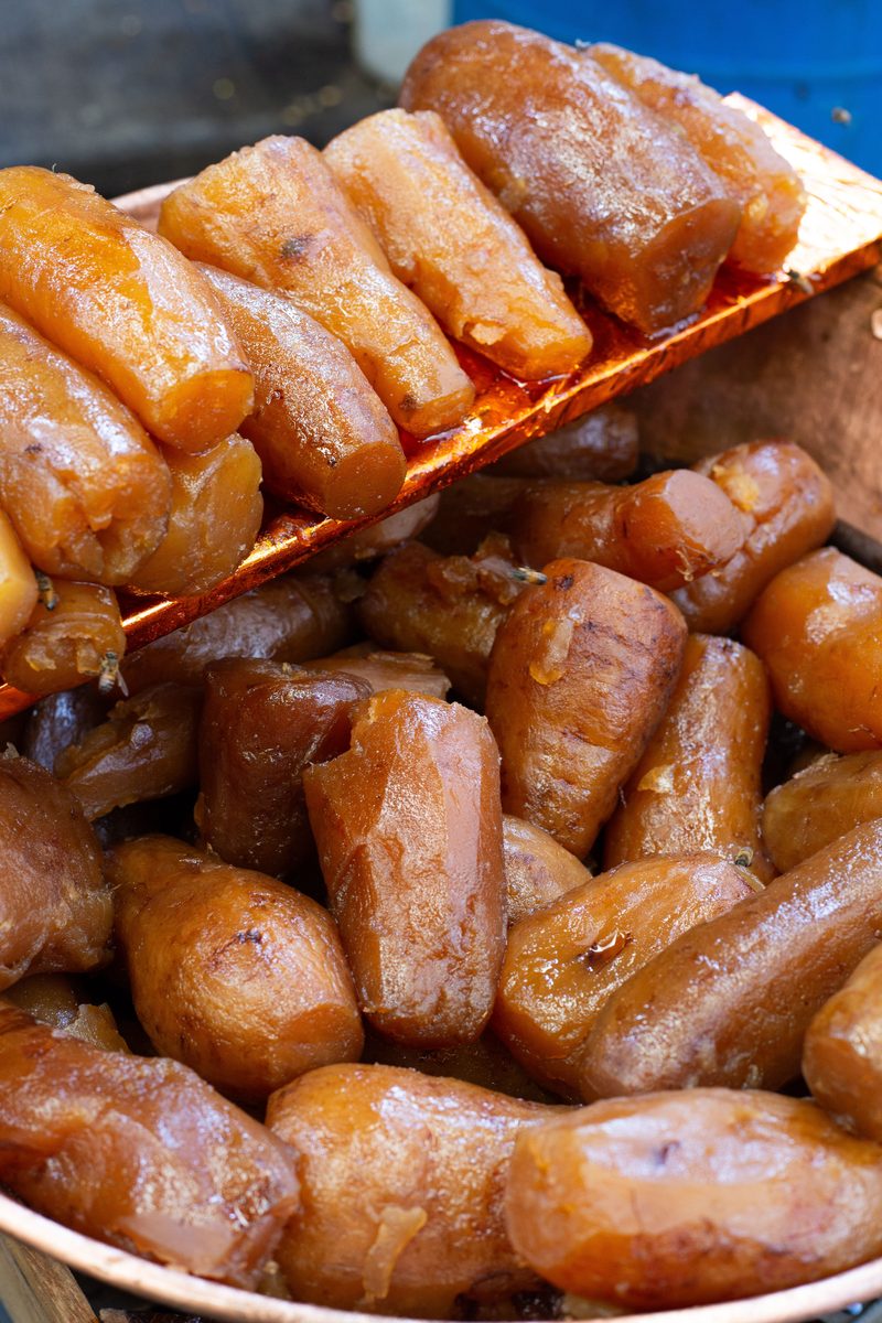 Glossy caramelized candied sweet potatoes piled in a serving tray, photographed close up.