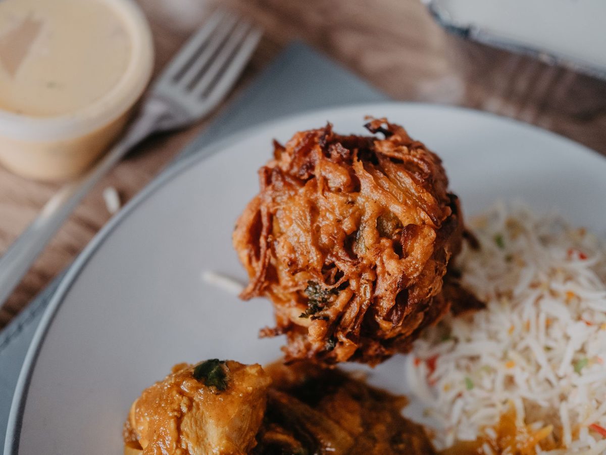Close-up of a golden-brown onion bhaji served with rice on a plate.