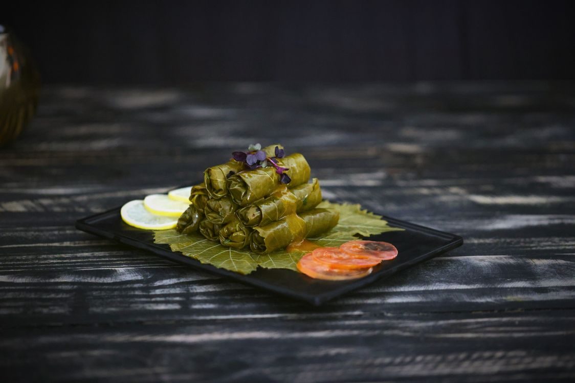 Finished dolma (stuffed grape leaves) served on a black plate with lemon garnish