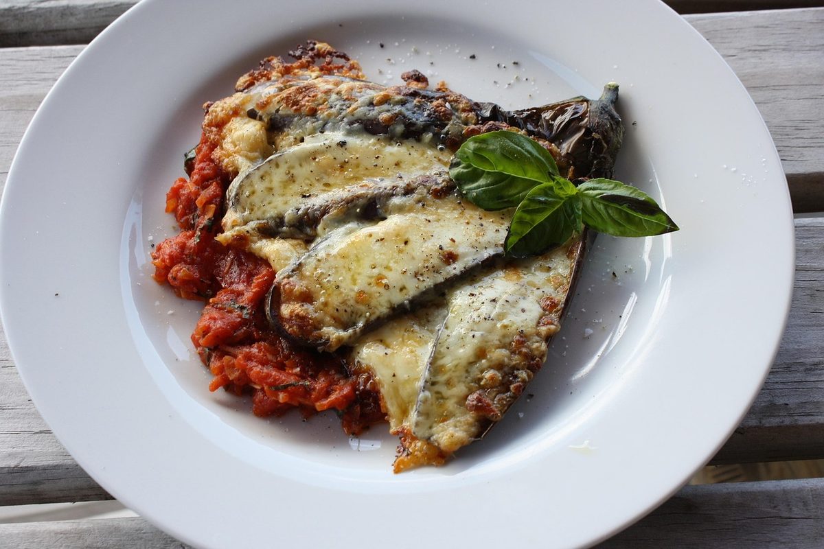 A plated serving of baked eggplant parmigiana layered with tomato sauce and melted cheese, garnished with fresh basil.