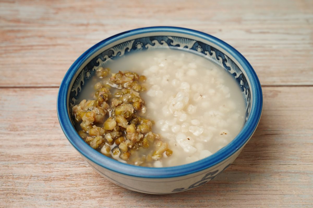 Close-up of mung bean and rice porridge in an ornate blue-and-white ceramic bowl on a wooden surface.