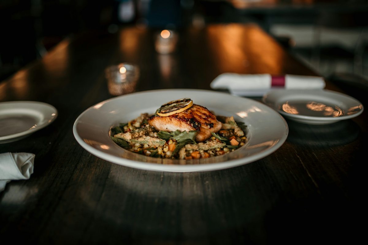 A finished restaurant dish of seared fish served over white beans with seafood garnish on a white plate.