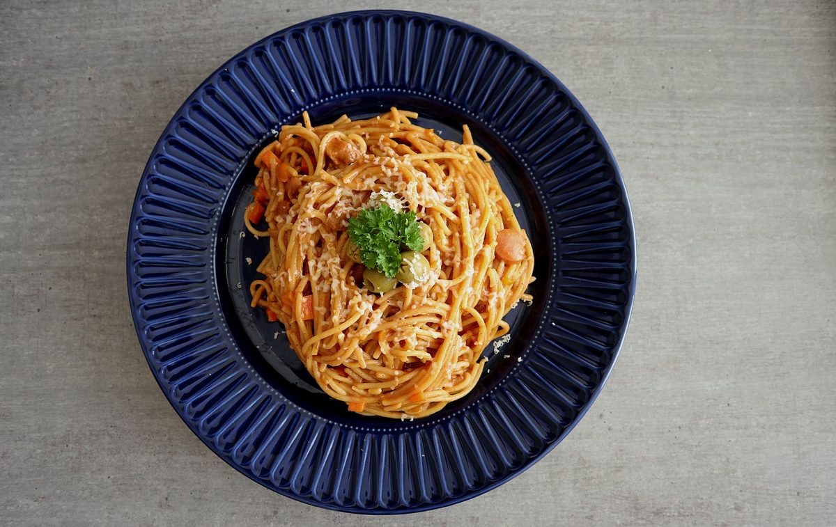 Finished Filipino-style spaghetti topped with cheese and parsley on a blue plate