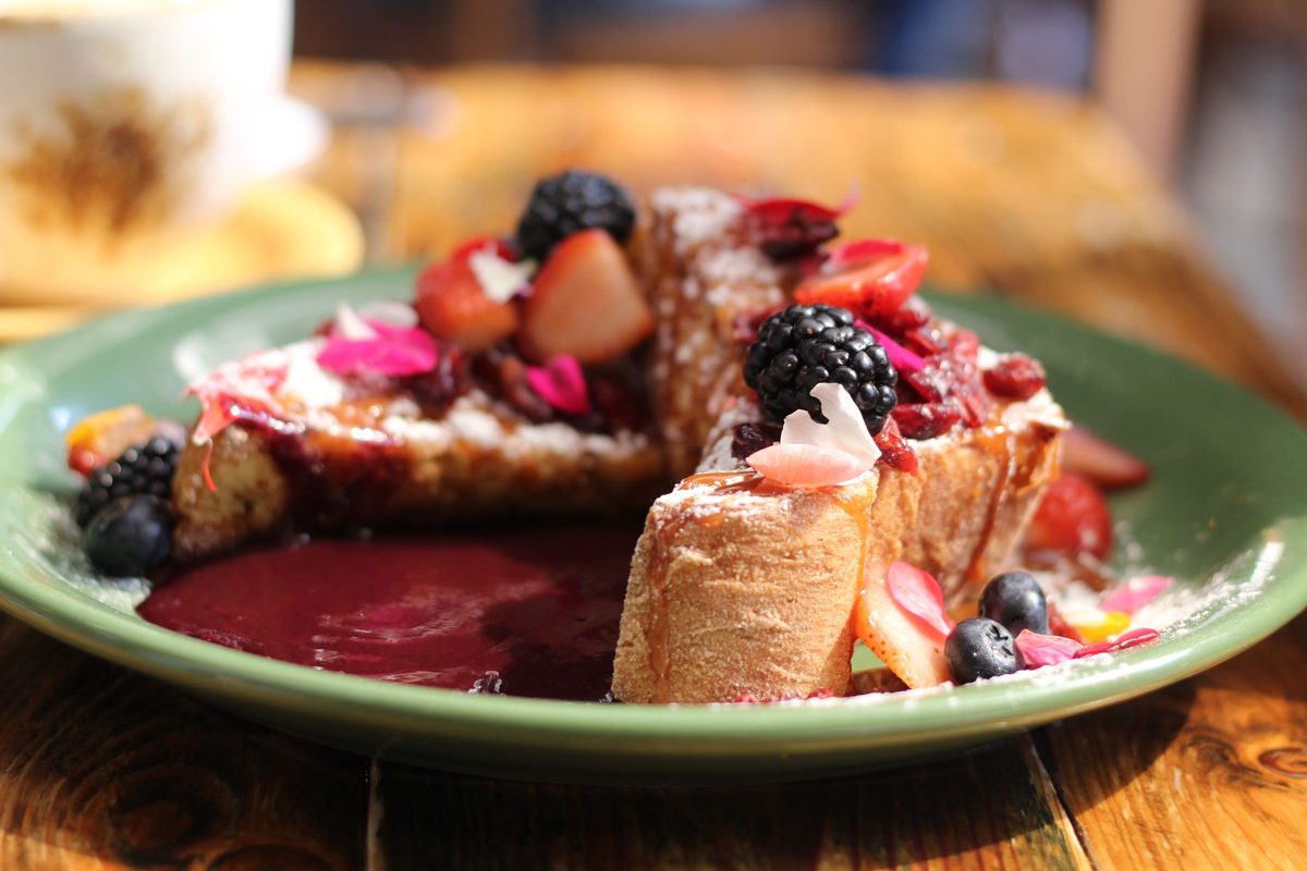 Finished French toast topped with fresh mixed berries and syrup on a green plate