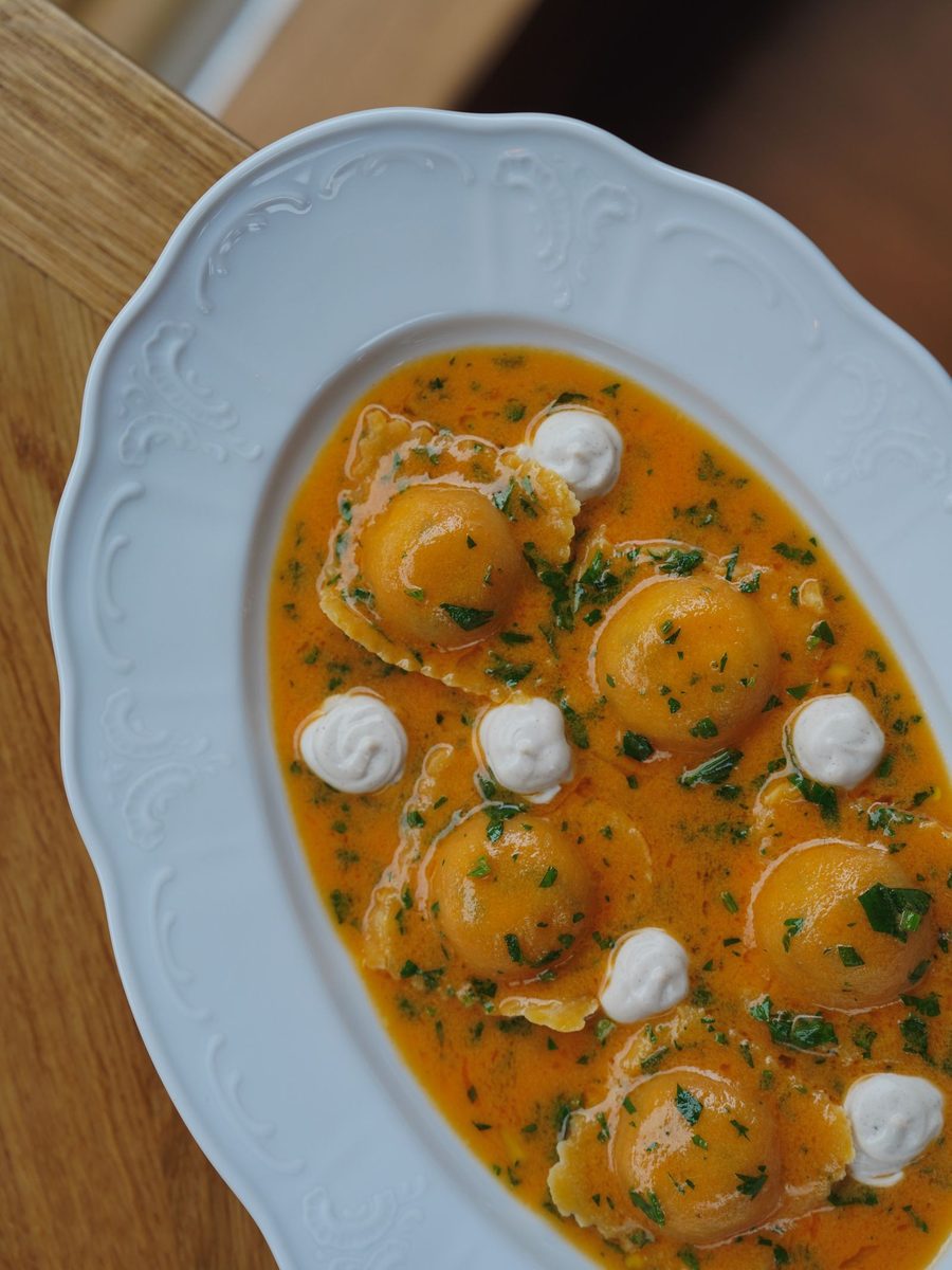 A plate of ravioli in creamy orange sauce, garnished with fresh herbs.