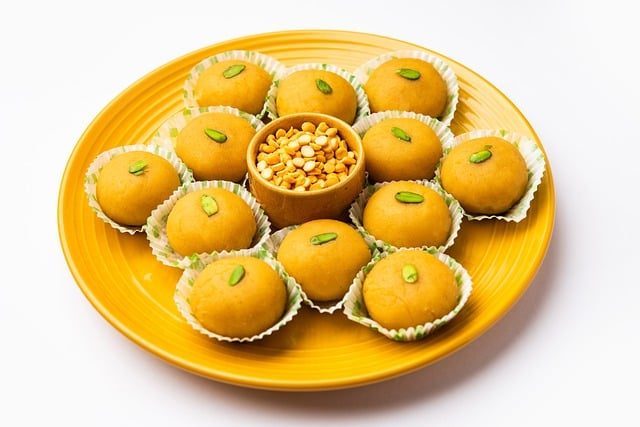 Plate of round golden Indian sweets garnished with pistachios and arranged around a small bowl of chopped nuts.
