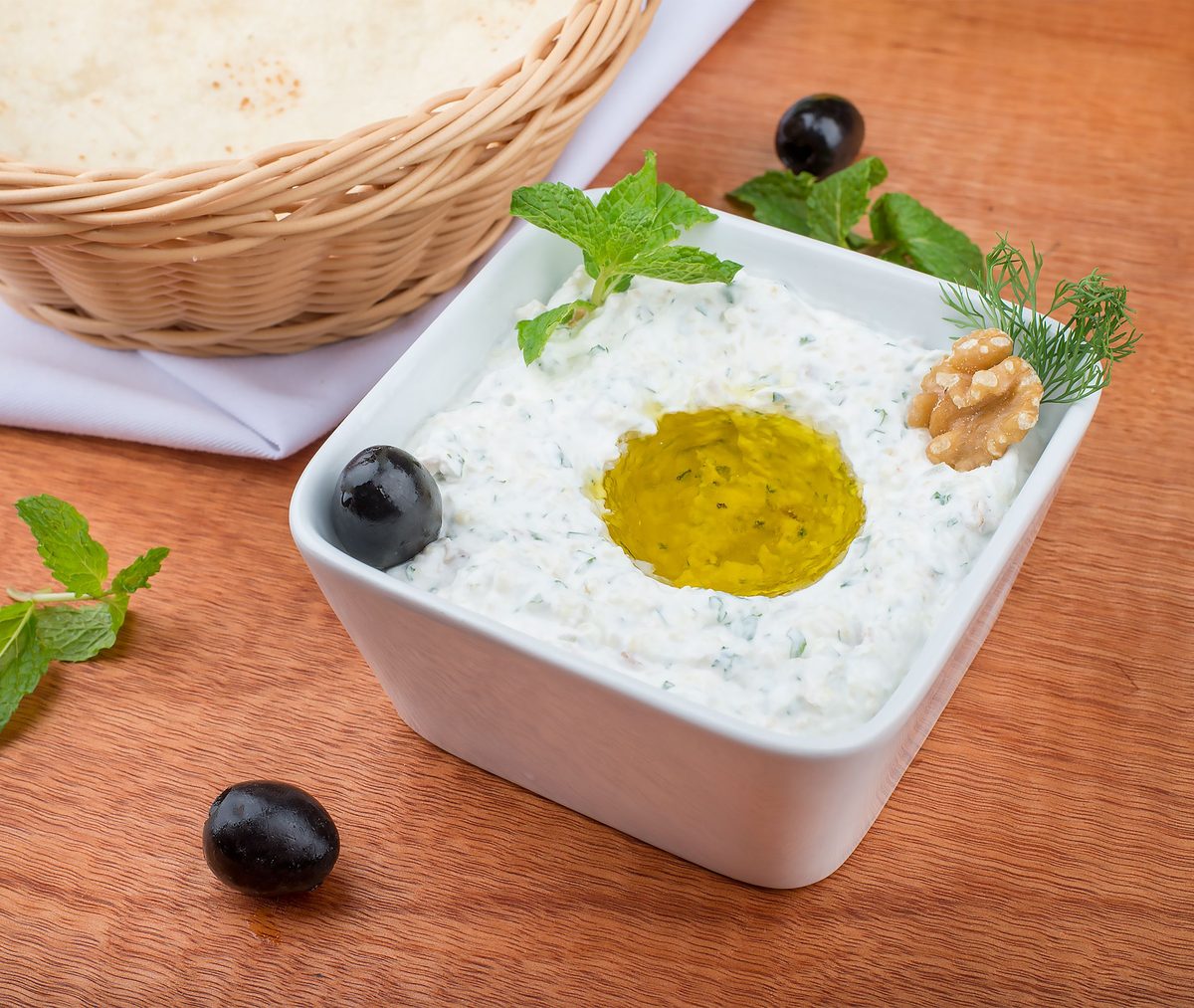 Finished Greek yogurt sauce in a ceramic bowl, garnished with olives, mint, and walnuts