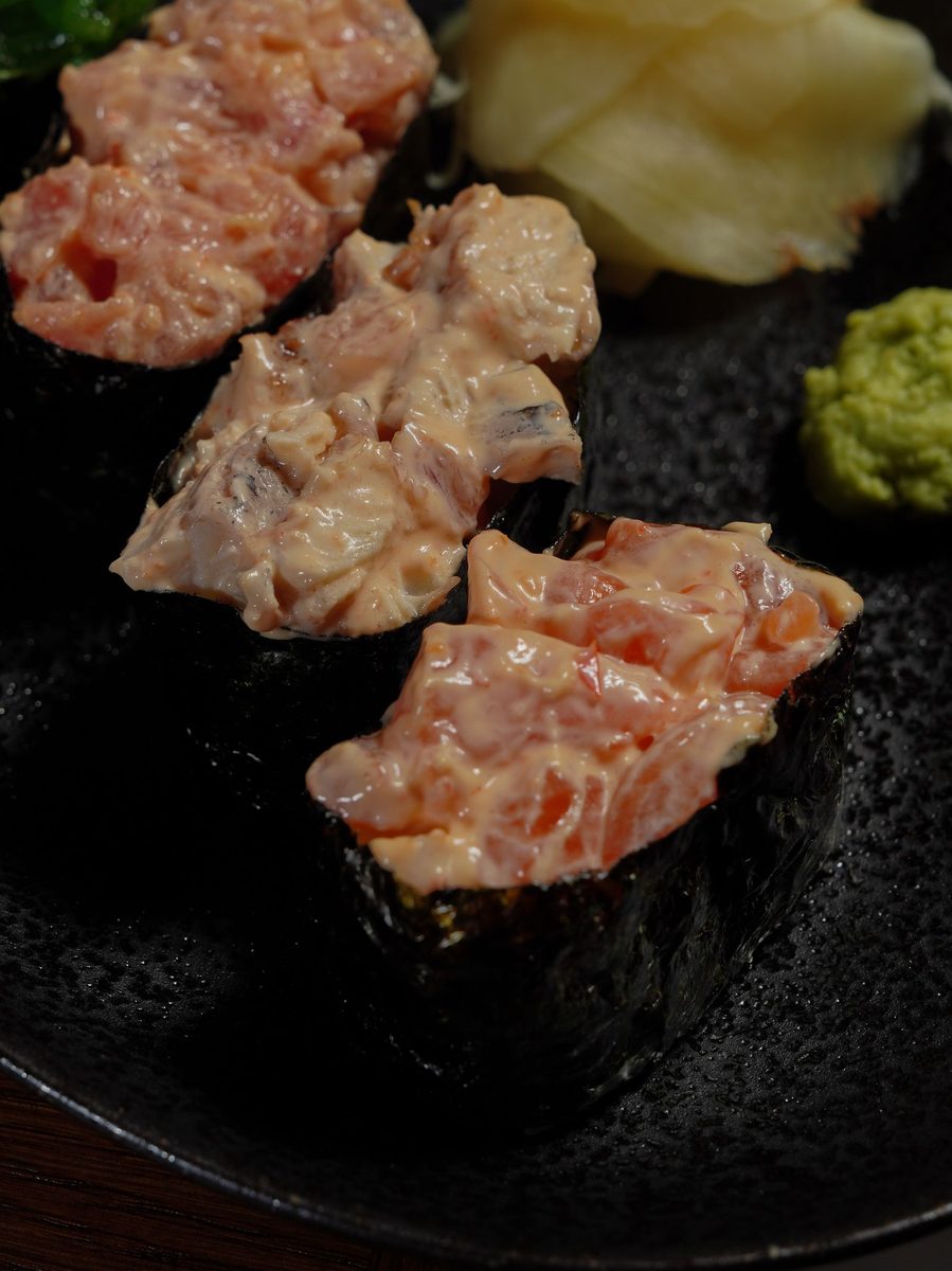 Finished gunkanmaki topped oval sushi with nori-wrapped rice and spicy salmon topping