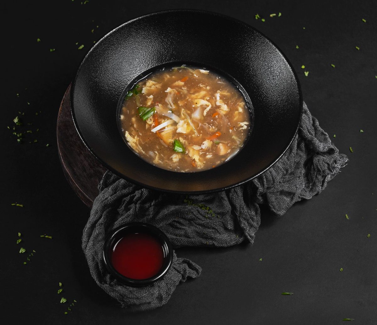 Finished Chinese hot and sour soup garnished with fresh herbs in a black bowl