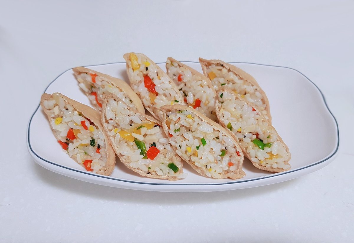 Finished Japanese inarizushi: sliced seasoned tofu pockets filled with colorful sushi rice, arranged on a white plate.