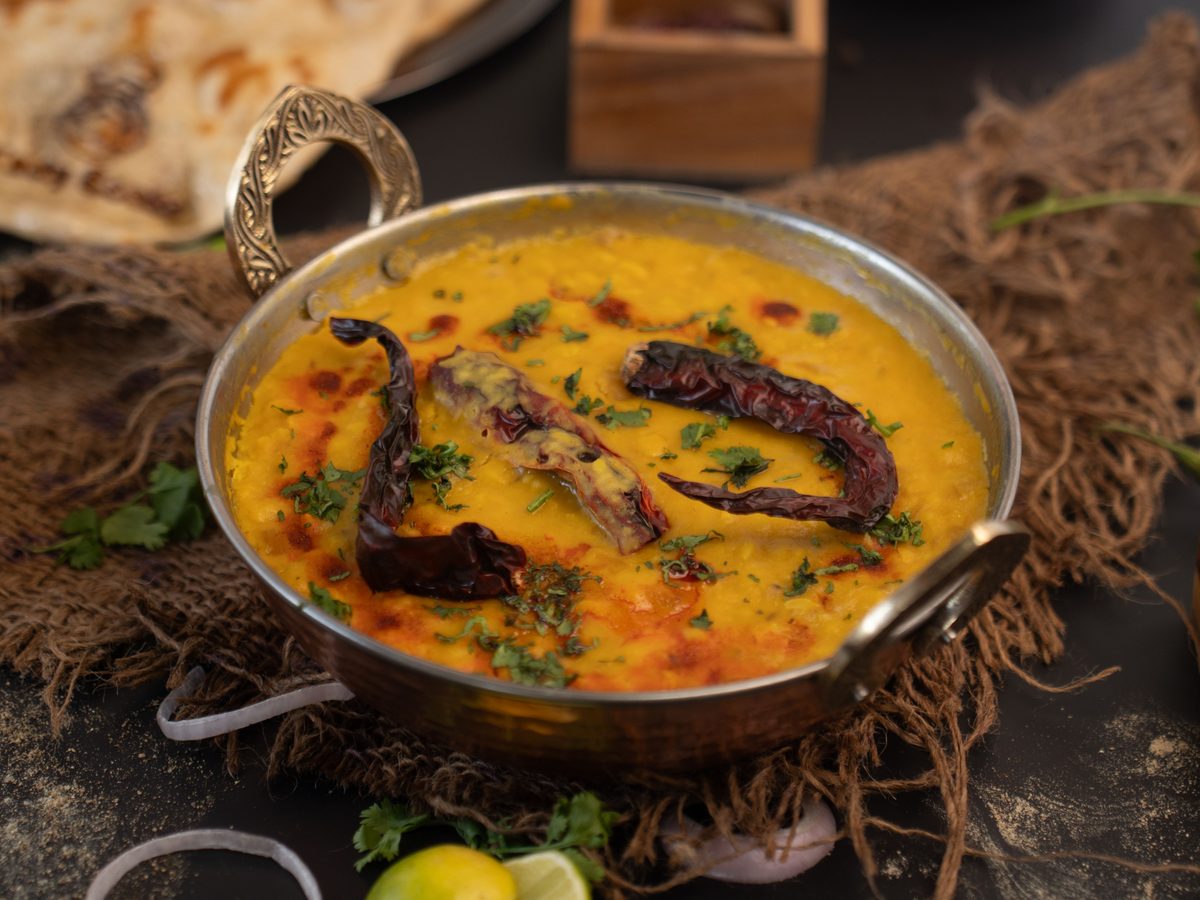 A bowl of finished golden-yellow Hyderabadi dal garnished with fresh cilantro, served with rice and green chilies on a dark table.