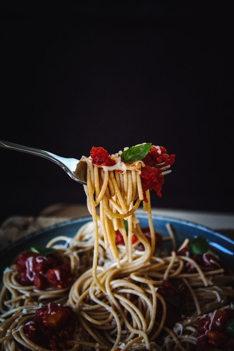 A close-up plated serving of spaghetti coated in red tomato sauce, garnished with fresh basil, with a fork beside the plate.