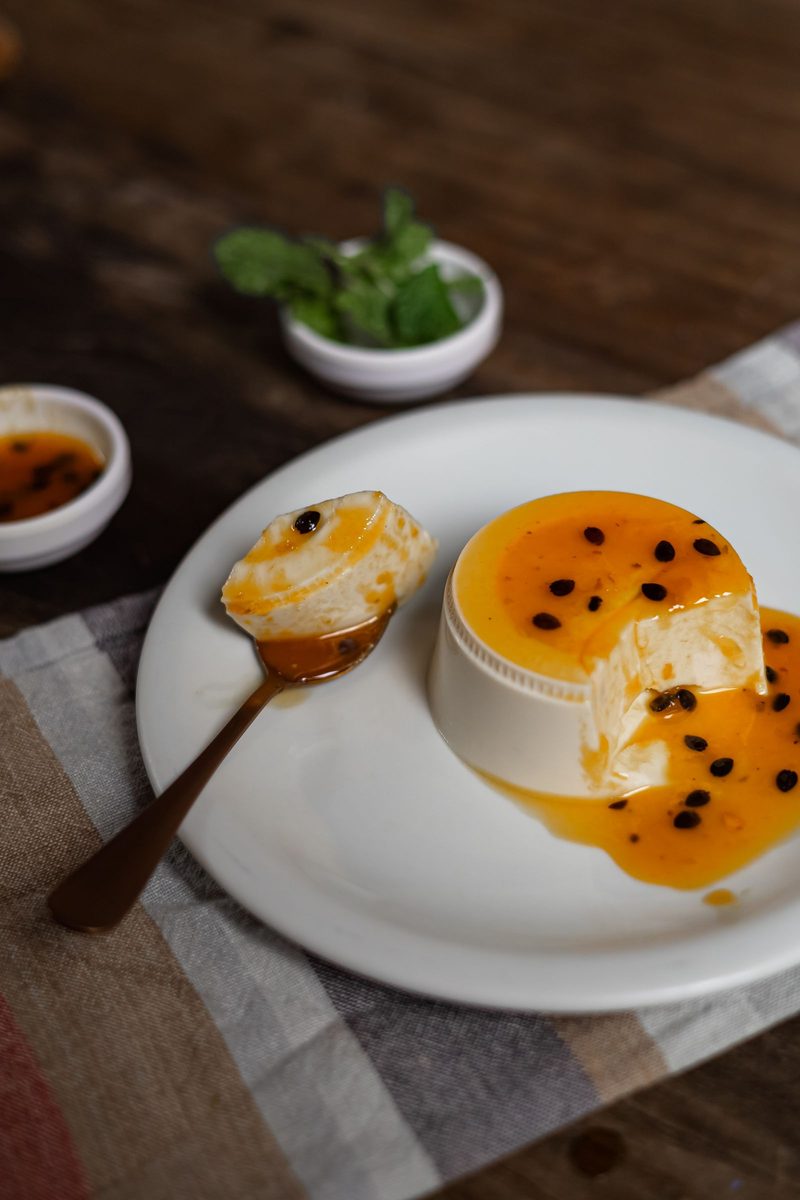 A square slice of caramel custard on a white plate, topped with glossy passion-fruit sauce.