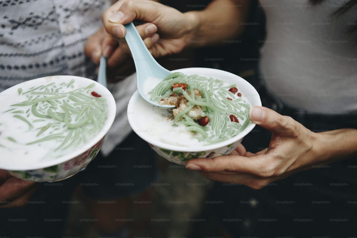 Finished bowl of green pandan noodle dessert with coconut milk and palm-sugar syrup, photographed as a Southeast Asian cendol-style sweet.