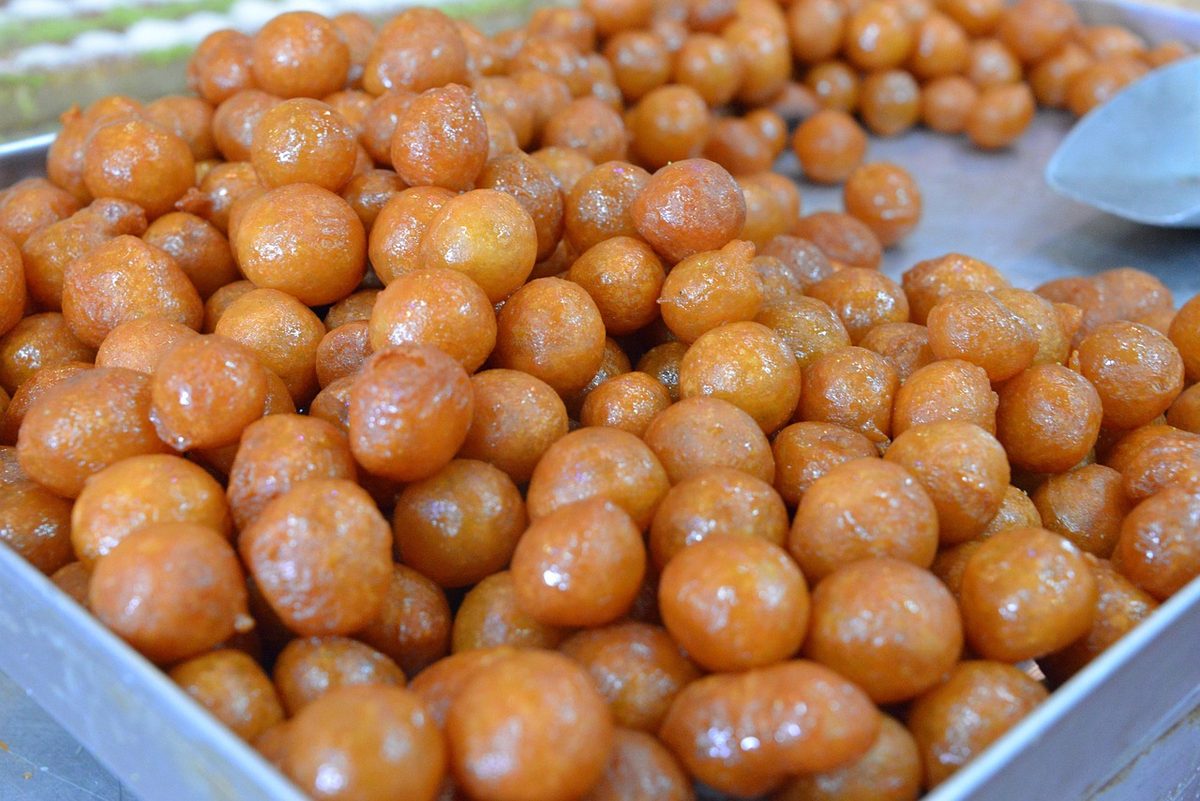 A bowl of golden loukamades (Greek honey donuts) drizzled with honey and sprinkled with pistachios.