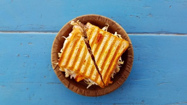 Overhead photograph of a toasted sardine sandwich cut into triangles on a small brown plate over a blue wooden table.