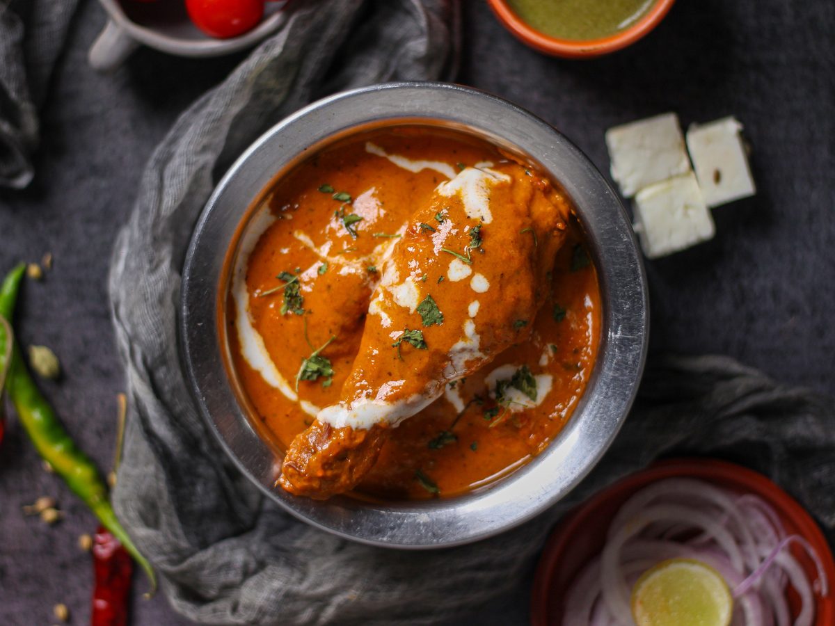 Overhead photograph of paneer butter masala, also called paneer makhani, in a bowl of creamy orange curry garnished with fresh herbs.