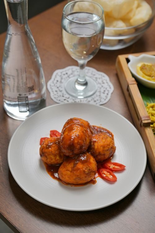 Finished dish of browned eggs coated in glossy reddish chili sauce, plated with sliced red chilies on a white plate.