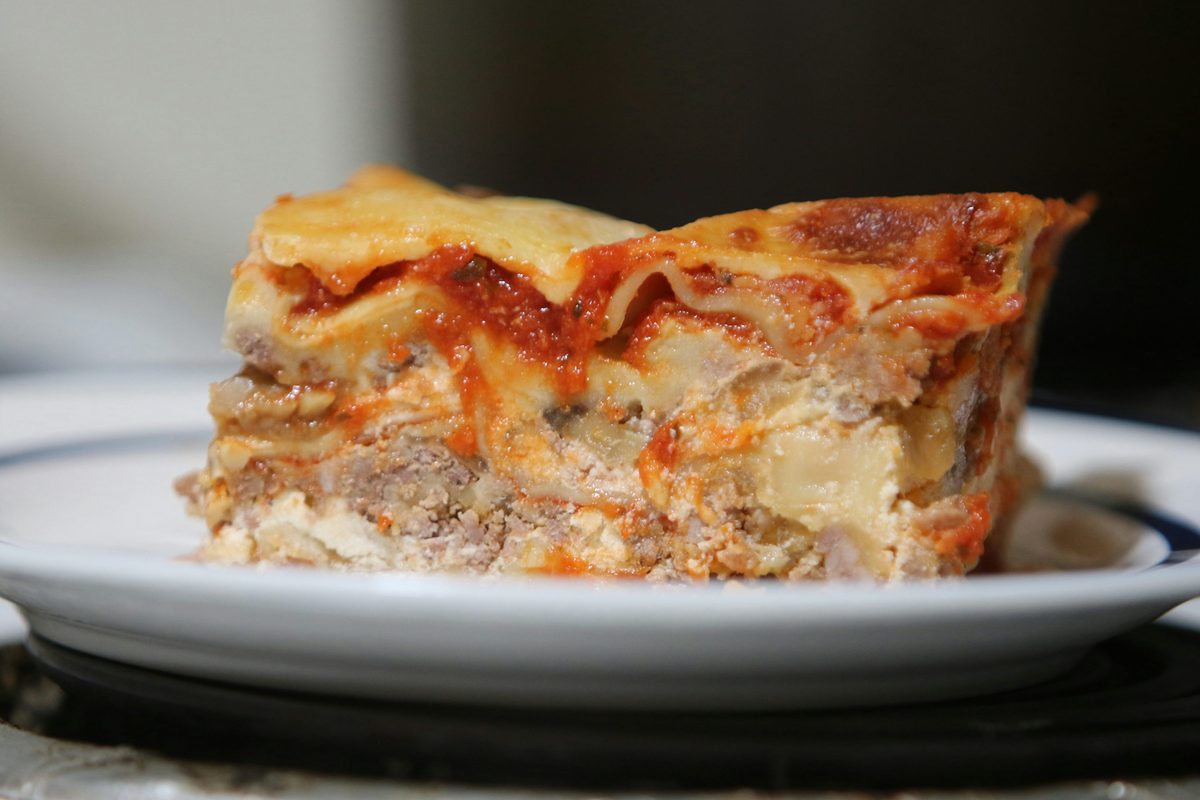 A close-up slice of baked lasagna with tomato sauce, layered pasta, meat, and creamy cheese on a white plate.