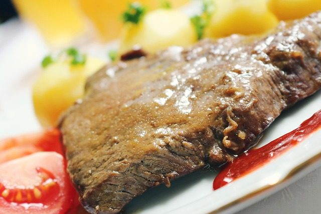 Sliced roast beef covered in gravy and served with potatoes and vegetables on a plate