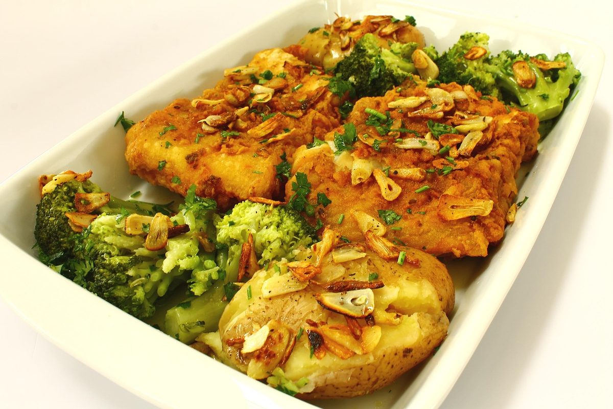 Finished Portuguese codfish dish with golden roasted cod portions, punched potatoes, broccoli, parsley, and sliced garlic arranged in a white serving dish.
