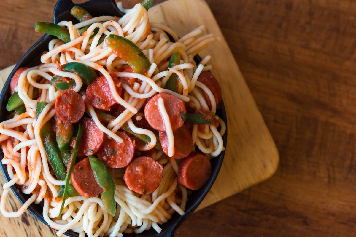 A bowl of spaghetti with green peppers and sliced sausages, served as a finished meal.
