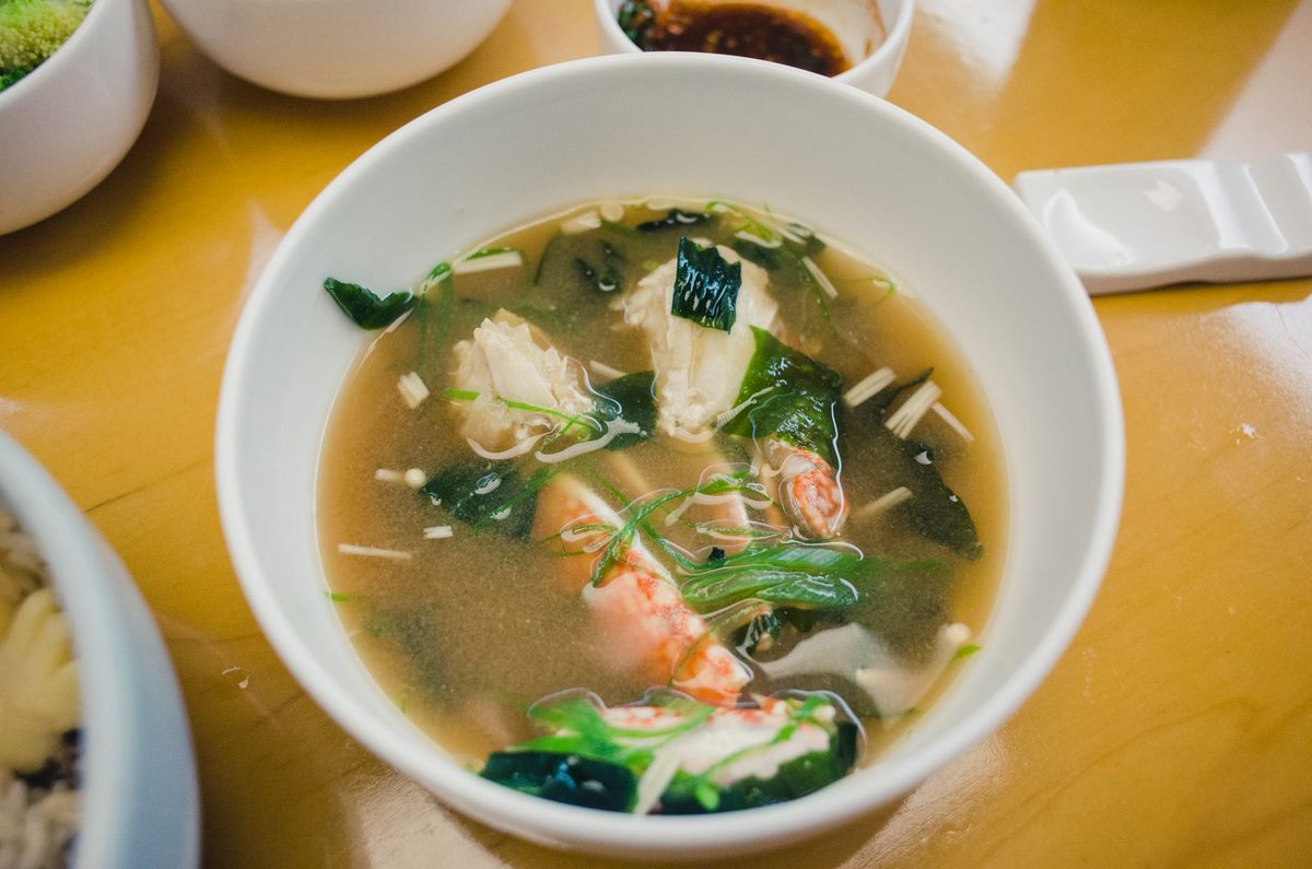 Close-up of a bowl of Japanese miso soup with tofu, seafood, and fresh greens in a ceramic bowl.