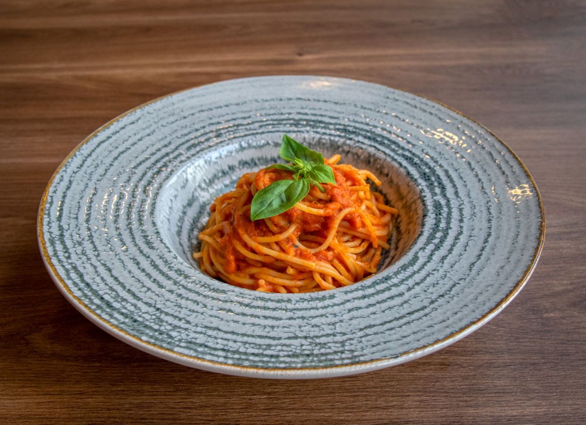 A plated serving of spaghetti in red tomato sauce, topped with fresh basil, on a wide patterned ceramic plate over a wooden table.