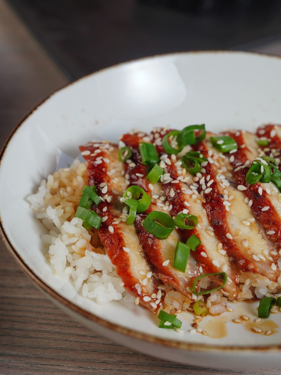 Close-up of a teriyaki chicken rice bowl topped with sesame seeds and sliced spring onions.
