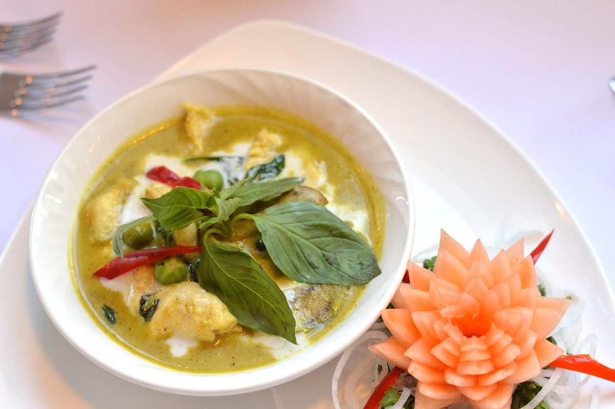 Bowl of Thai green curry with chicken pieces, vegetables, red chilies, and fresh basil