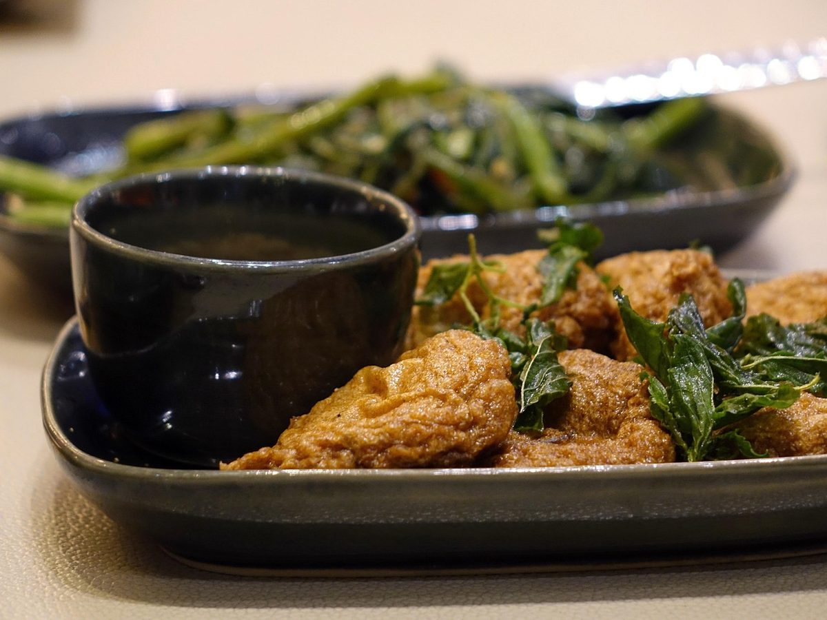 Golden-brown Thai fish cakes served with red dipping sauce on a white spoon, with a lime wedge and herbs beside them