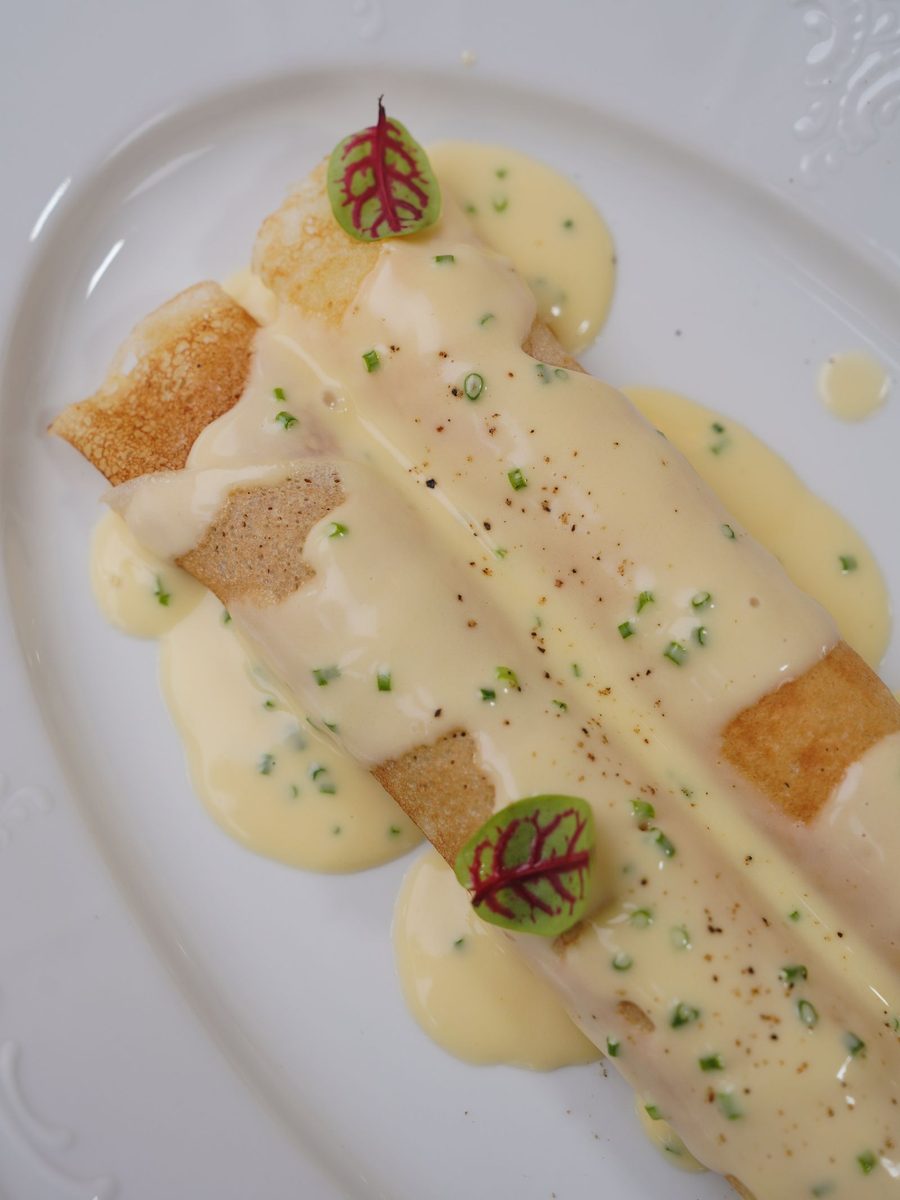 Rolled crepes drizzled with creamy melted cheese and herbs on a white plate.