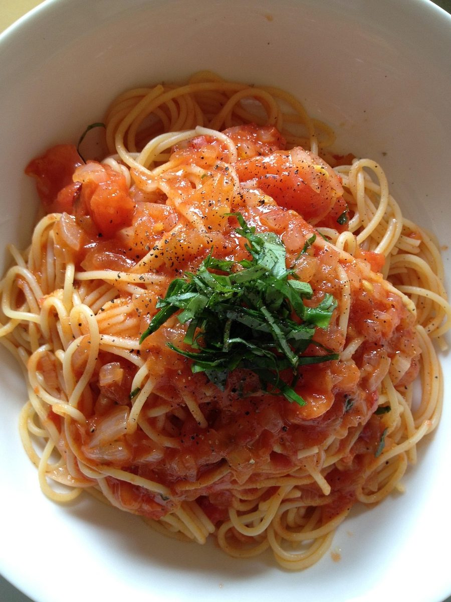 Close-up of spaghetti topped with chunky tomato sauce, chopped herbs, and black pepper in a white bowl.