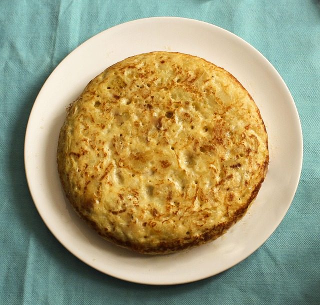 Whole golden Spanish potato omelette (tortilla española) on a white plate over turquoise cloth.