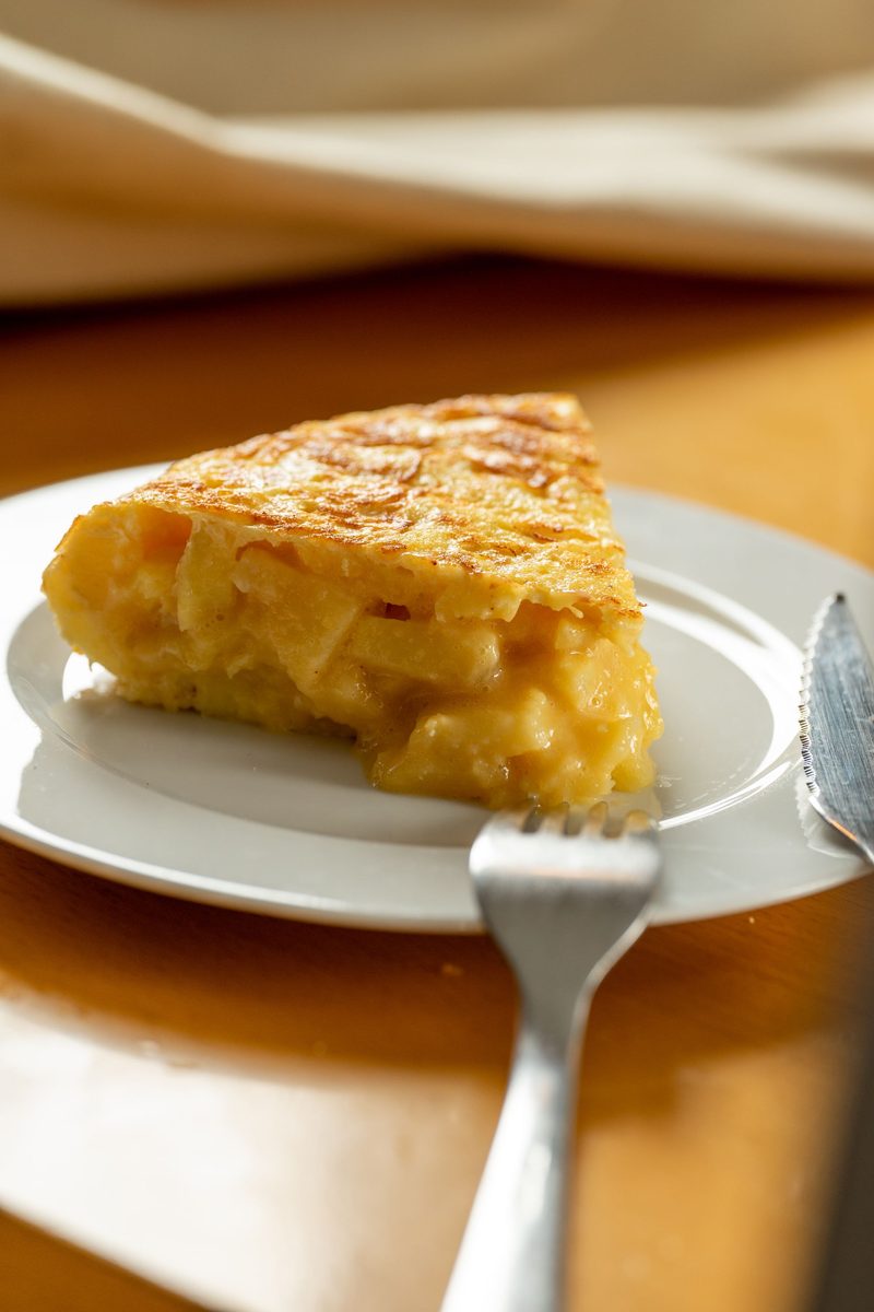 Appetizing slice of Spanish potato omelette (tortilla española) on a white plate.