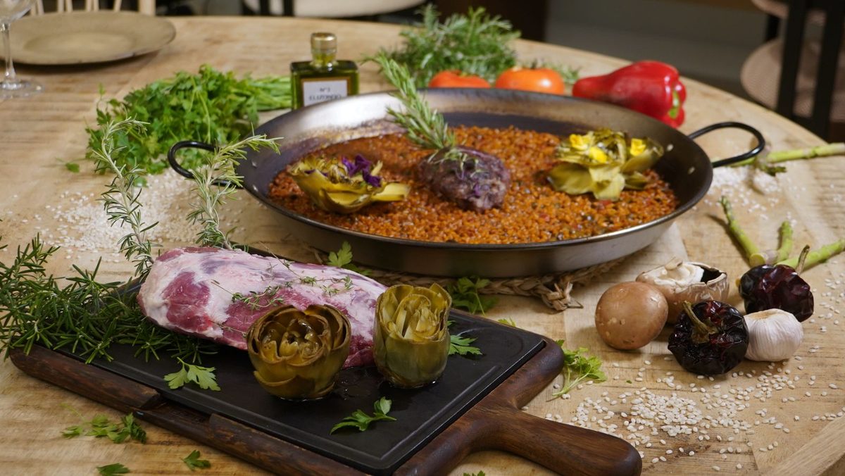 Finished Valencian-inspired paella with browned meat, artichokes, and fresh vegetables in a paella pan