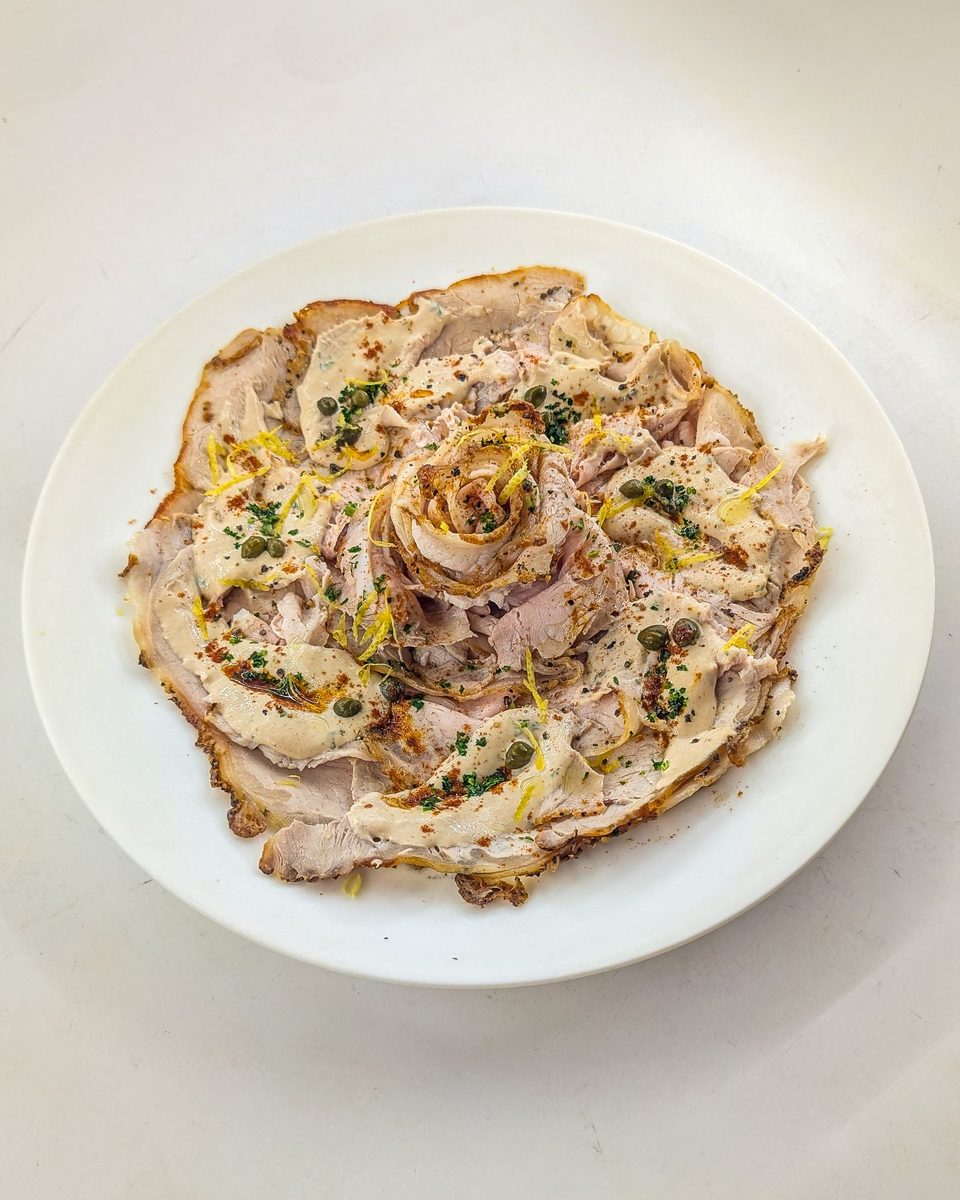 Sliced vitello tonnato arranged as an elegant plated dish, covered with creamy tuna sauce and garnished with capers.